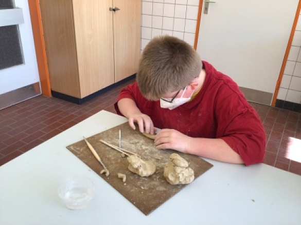 Ein Junge sitzt am Tisch und formt mit seinen Händen die Tonmasse. 