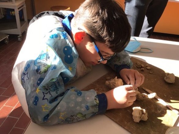 Ein Junge sitzt am Tisch und formt mit seinen Händen die Tonmasse. 