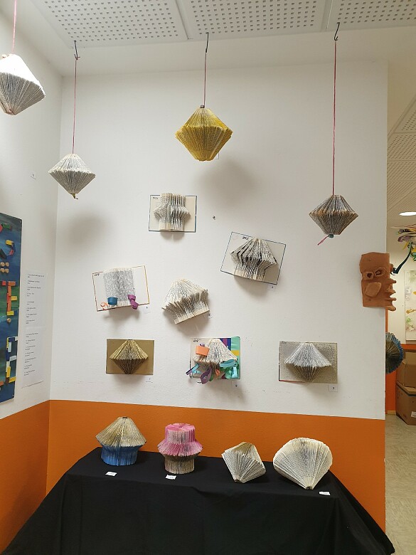 Kreativ gestaltete Bücher hängen von der Decke und sind auf einem Tisch ausgestellt. 