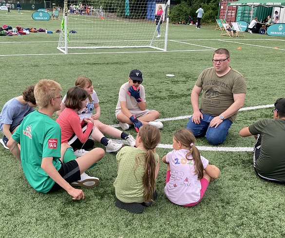 Herr Haller sitzt mit sechs Schüler:innen der GDS auf dem Boden. Sie besprechen die nächsten Spielzüge. 