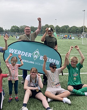 Herr Haller steht mit fünf Schüler:innen zusammen. Sie halten die Medaillen hoch. 