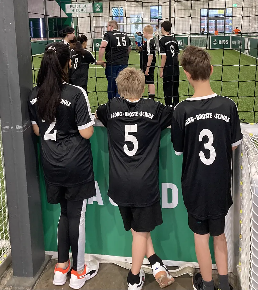 Schüler:innen auf dem Spielfeld und vor dem Spielfeld. 