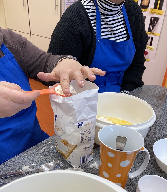 Eine Lehrerin streift von einem speziellen Löffel (Messlöffel) das Mehl mit dem Finger runter. 