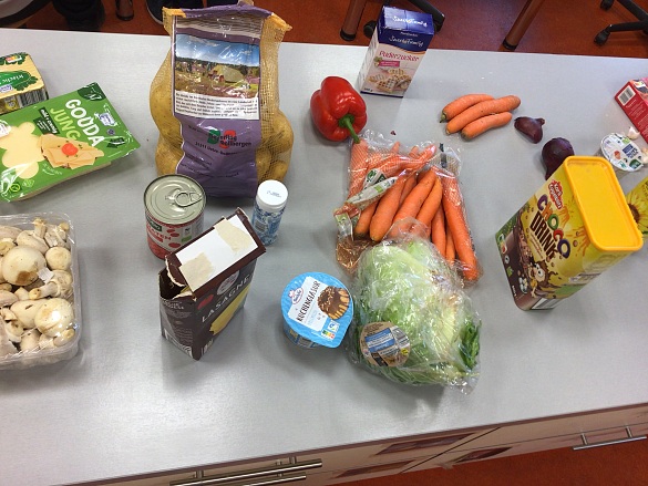 Die Zutaten zum Kochen liegen auf dem Tisch: Käse, Champignons, Kartoffeln, Paprika, Möhren, Puderzucker, Schokoglausur, Salat, Kakaopulver, Zwiebeln.