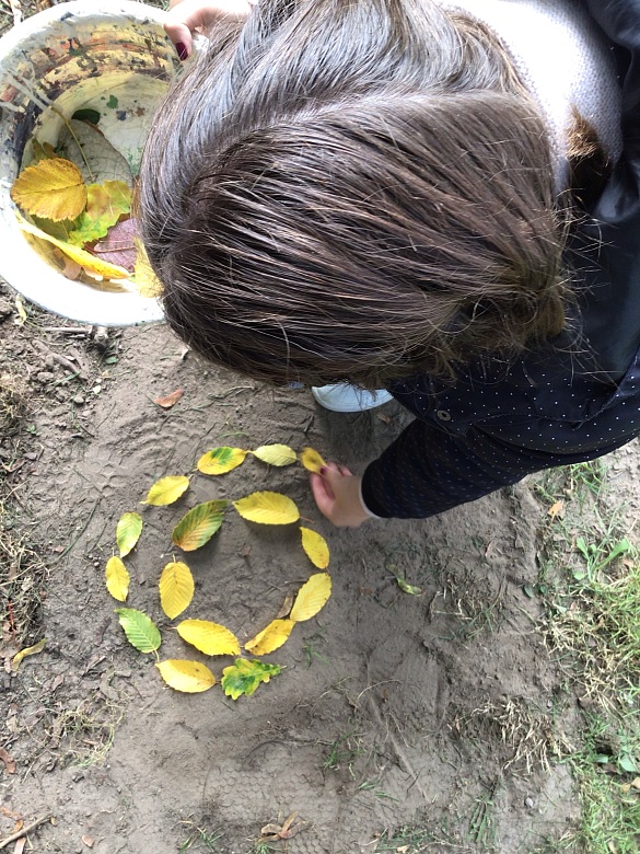 Ein Mädchen legt die Blätter kreisförmig auf den Boden. 