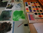 auf dem Bild sind mehrere Tuschkästen und farbig grundierte Papiere.