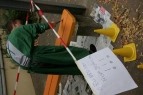 Zu sehen ist ein Schüler mit Kunstkittel, der eine Bank auf dem Schulhof mit oranger Farbe anstreicht.
