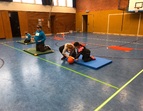 Drei Schüler:innen beim Goalballspielen. FSJlerin unterstützt bei der Ballführung. 