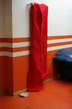 Auf dem Bild ist ein in rotem Filz verpackter, hochkanter Heizkörper zu sehen, der sich in Foyer des Schulgebäudes befindet. Rechts daneben befindet sich ein blaues Sofa. 