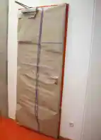 Zu sehen ist eine in grauem Packpapier verhüllte Tür, die mit einem lilafarbenen Band verziert ist.